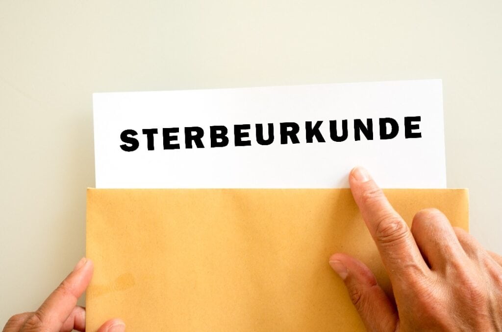 Eine Hand nimmt eine Sterbeurkunde aus einem Briefumschlag