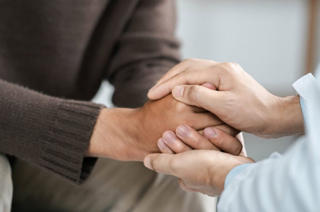 Männliche Ärzte schütteln Patienten die Hand, ermutigen sich gegenseitig und beten um Segen. Liebe, Fürsorge und Ermutigung anbieten, während sie den Gesundheitszustand des Patienten überprüfen. Konzept der Medizin